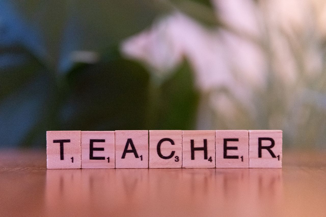 The Art of Drawing Readers In: Your attractive post title goes here Close-up of wooden tiles spelling 'Teacher' on a table, conveying education and learning.