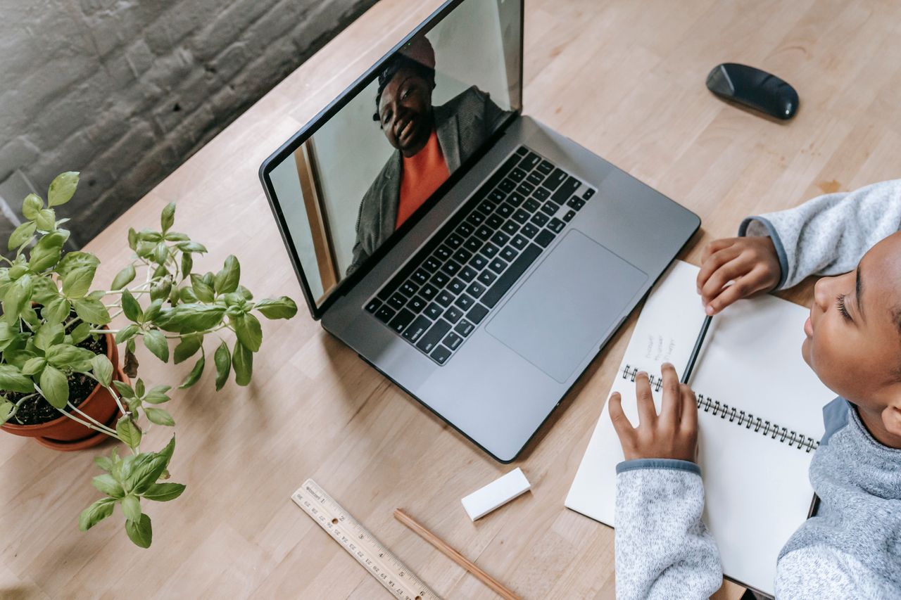 our-values Top view of adorable intelligent African American boy preparing for exam with tutor through internet on latop