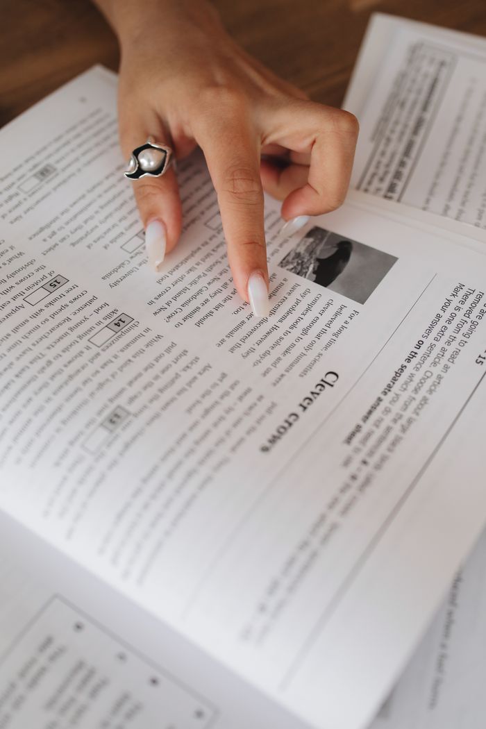 services-05 A hand with a ring points at text in an open book, suggesting reading or studying.