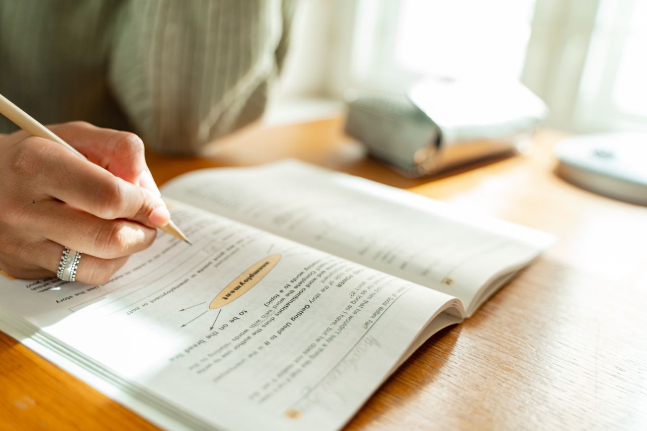 embark A student takes notes while studying at a sunlit desk with an open textbook.